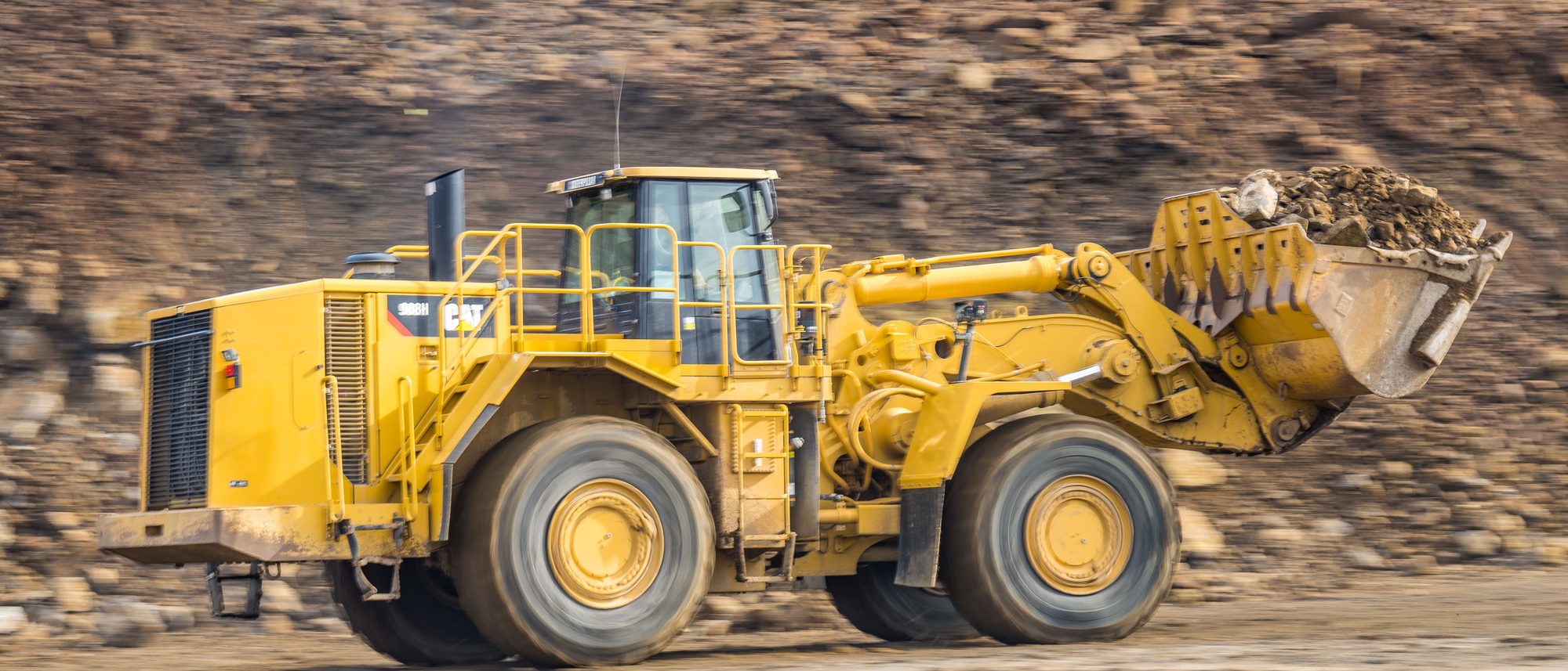 A wheel loader moving at speed across a quarry floor, trailing dust